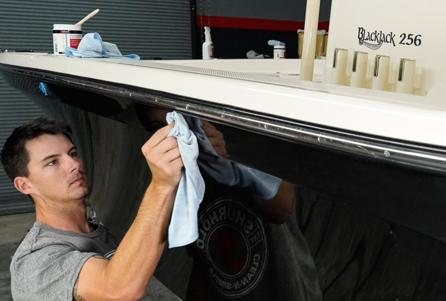 A man uses a cloth to clean the side of a Blackjack 256 boat inside a garage or workshop.