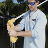 A person in sunglasses uses a Shurhold Industries, Inc. Water Sprite Deck Mop with superior absorption to wring water outdoors near a body of water, holding the mops white pole.
