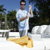 A person in sunglasses and a light blue shirt uses a Shurhold Industries, Inc. Water Sprite Deck Mop, known for superior absorption, to clean a white boat docked near palm trees.