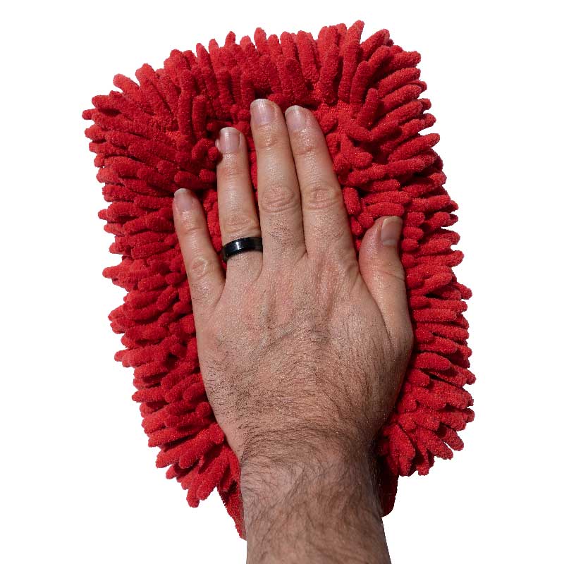 A hand with a black ring presses on a red Shurhold Industries, Inc. Chenille Microfiber Premium Scratch-Free Wash Mitt, showcasing its chenille fibers for gentle, scratch-free washing against a white background.