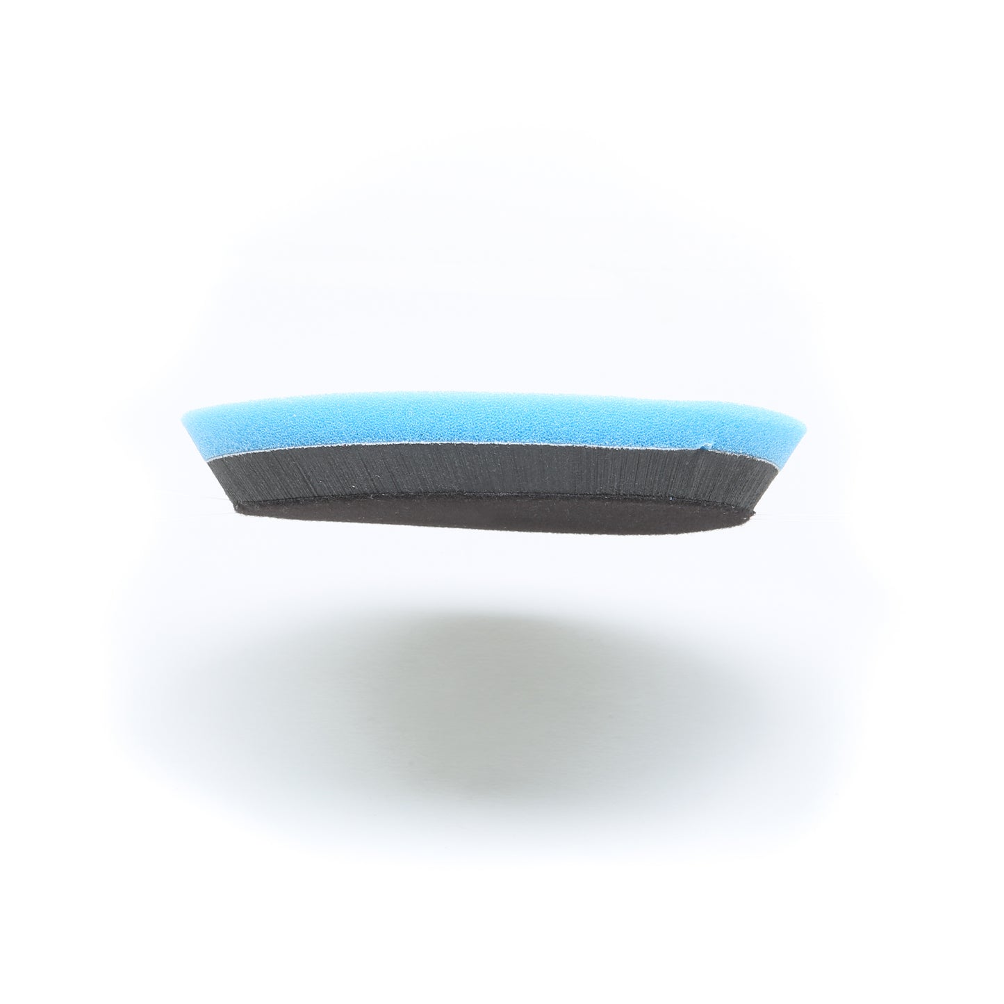 A close-up of the Shurhold Buff Magic Heavy Oxidation Pad shows its blue top and black bottom layers, designed to tackle severe oxidation when paired with the Buff Magic Heavy Cutting Pad, set against a white background.