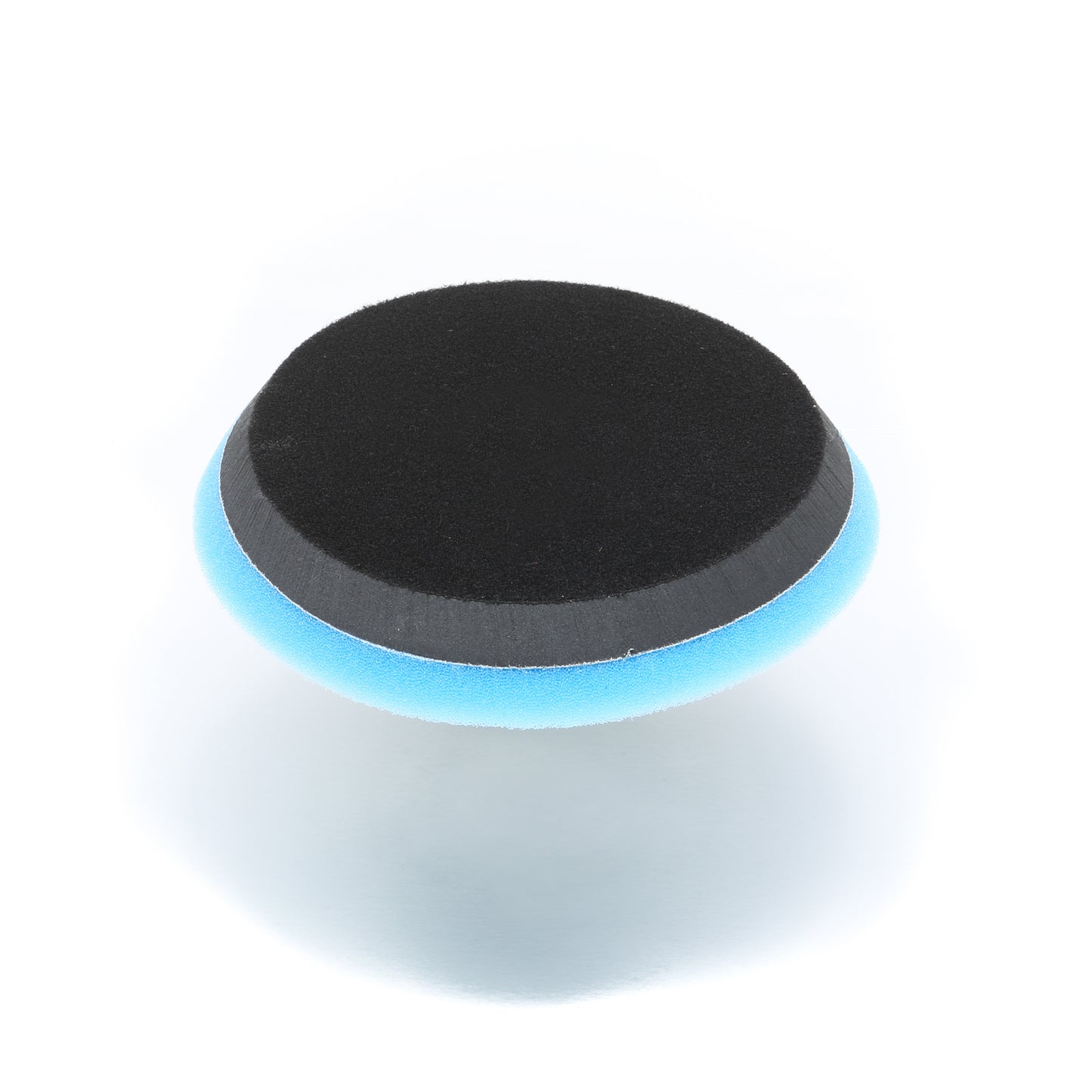 A round, two-layered sponge with a black top and blue bottom from Shurhold Industries, Inc., the Buff Magic Heavy Oxidation Pad is shown on a white background and is ideal for tackling severe oxidation during polishing.